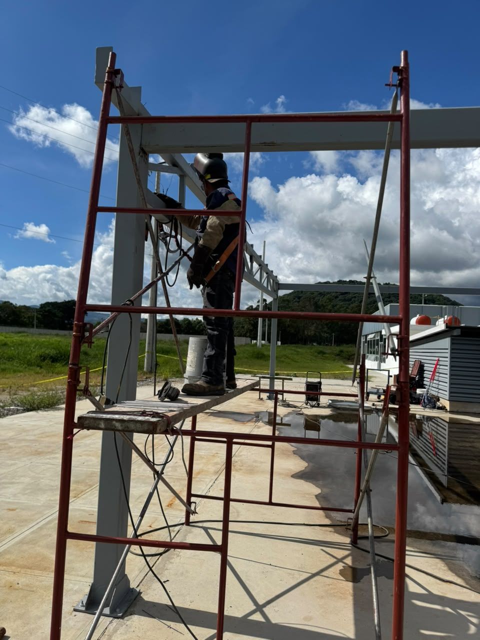 Soldador con arnés trabajando sobre andamio en una estructura metálica
